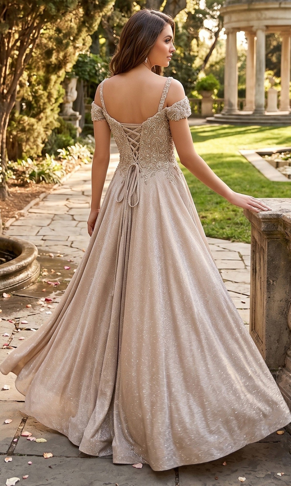 A woman wearing the Long Prom Dress: Chicas J169—featuring a shimmering, off-the-shoulder design, embellished bodice, and lace-up back—stands on a stone path in a garden surrounded by greenery and classical columns.